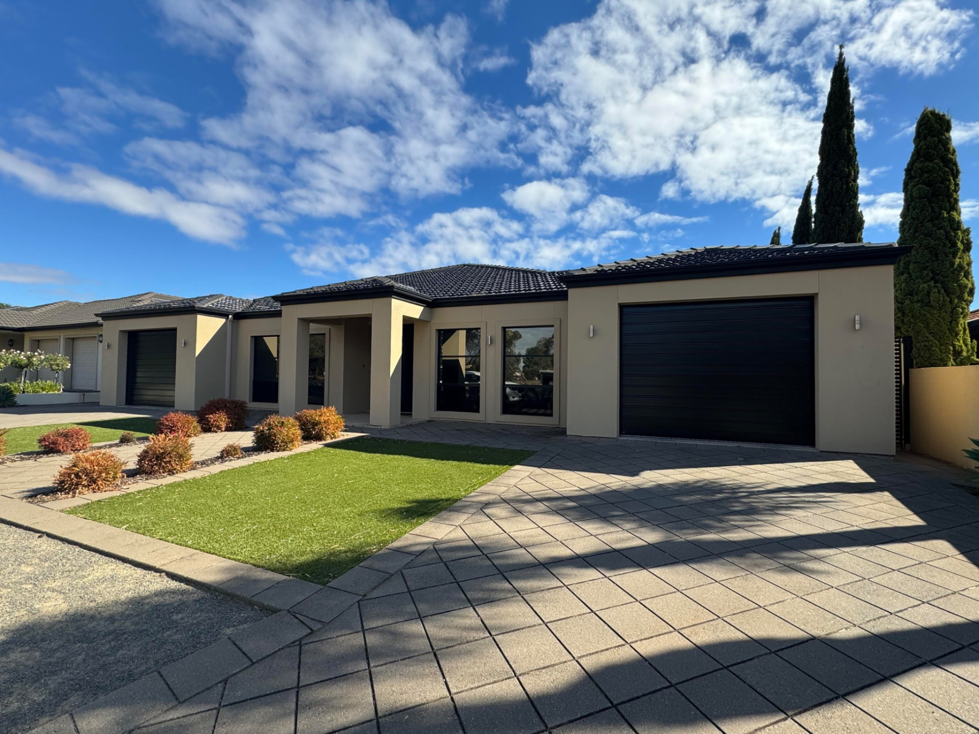 Modern rendered home with two black roller garage doors and a paved driveway