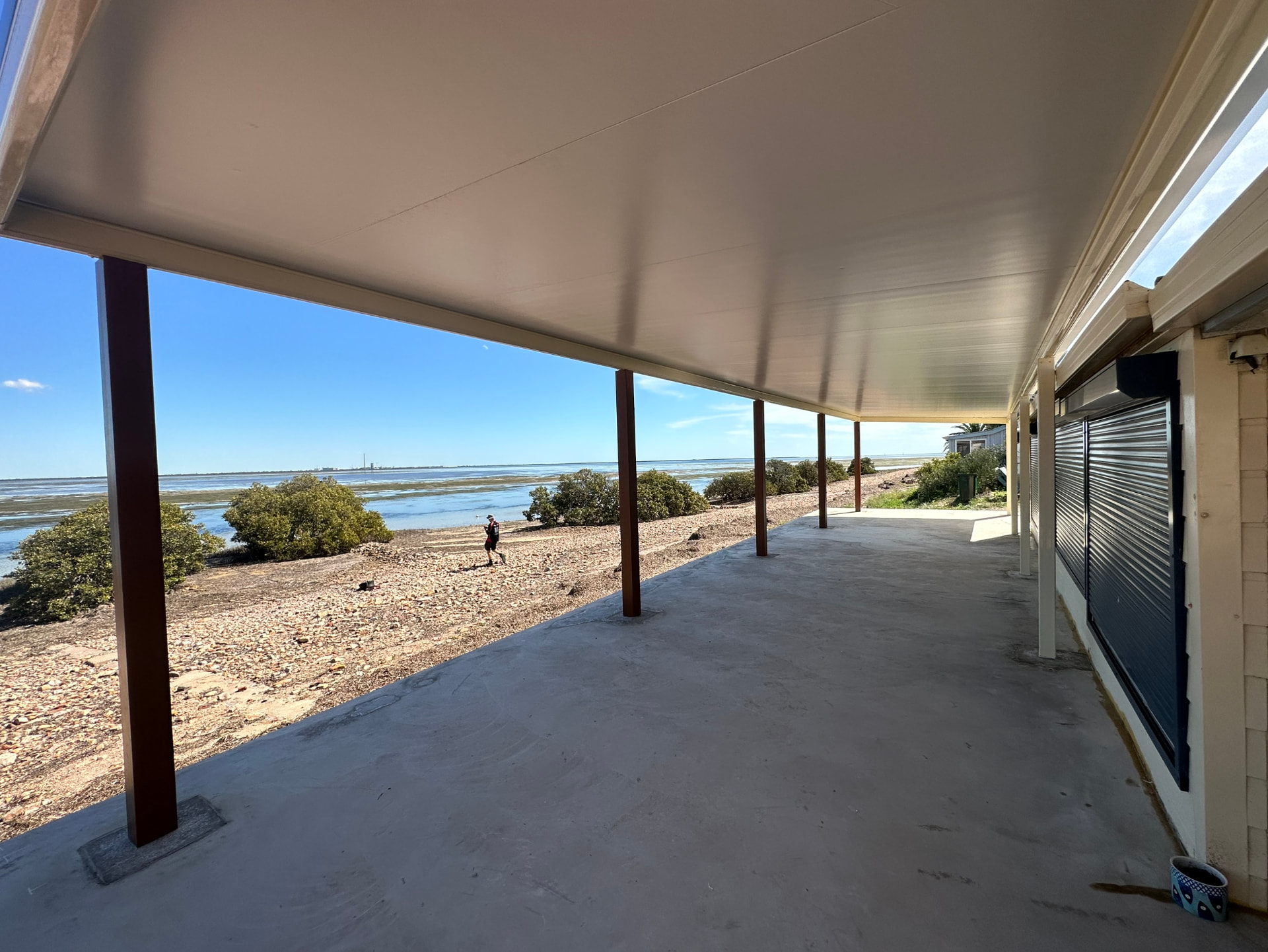 View out from under a Stratco Outback flat patio with Cooldek roof toward mangroves and water