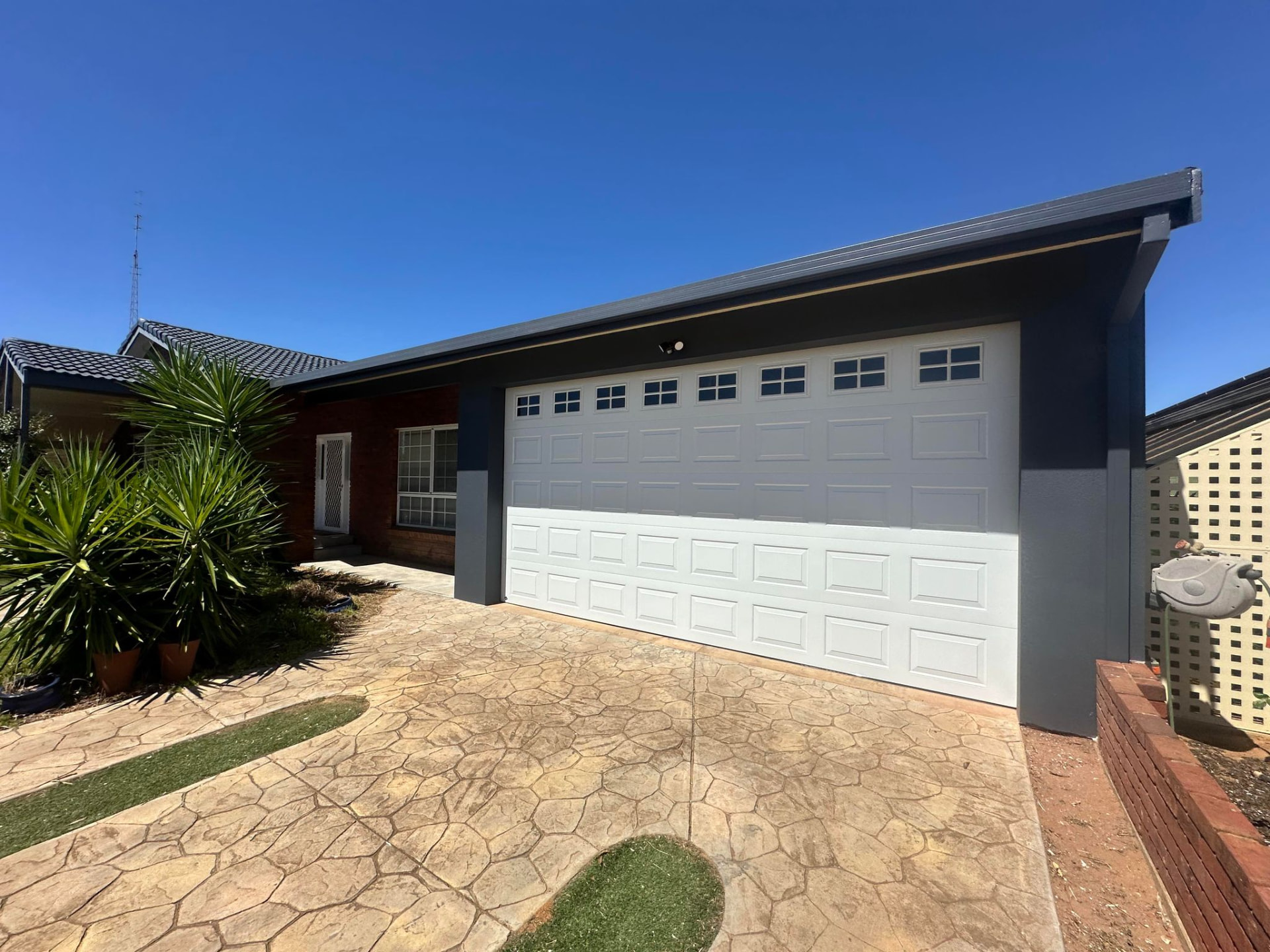 White panelled sectional garage door with window inserts on a home with a charcoal facade
